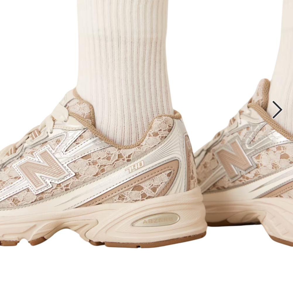 Beige sneakers with lace details worn with white socks on a white background